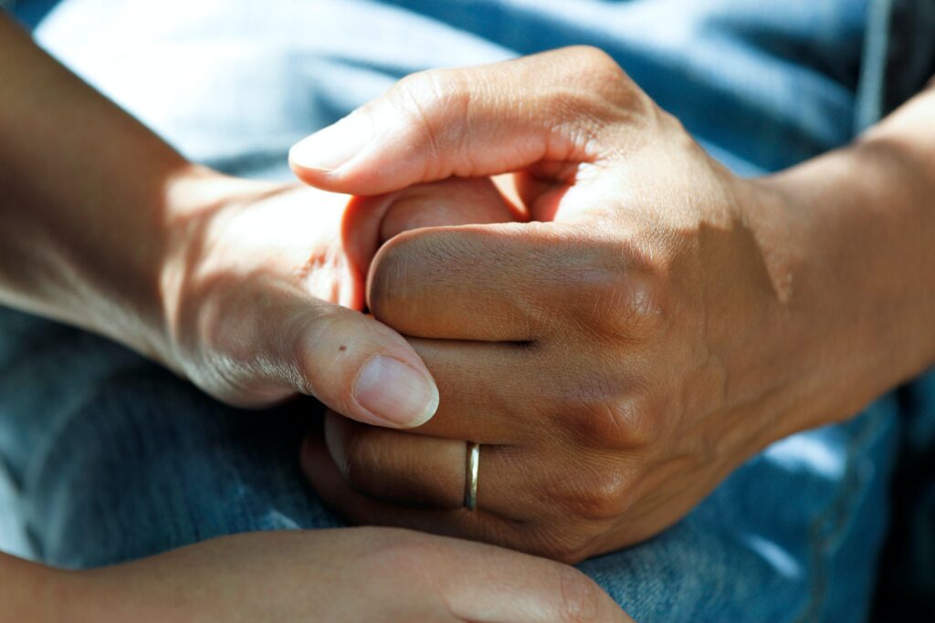 A dark skinned hand is holding the fair skinned hand of another person in a comforting grip
